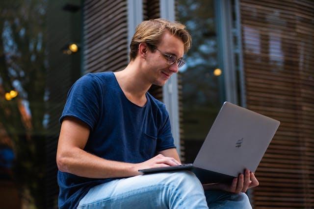 A man holding a grey laptop while sitting outside